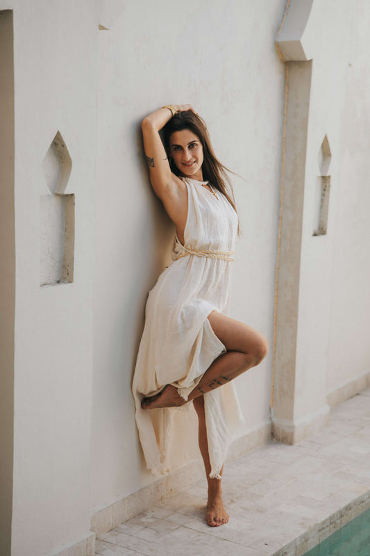Woman wearing the Delphi Dress — long organic crepe cotton dress with golden Eri silk braids and side slits