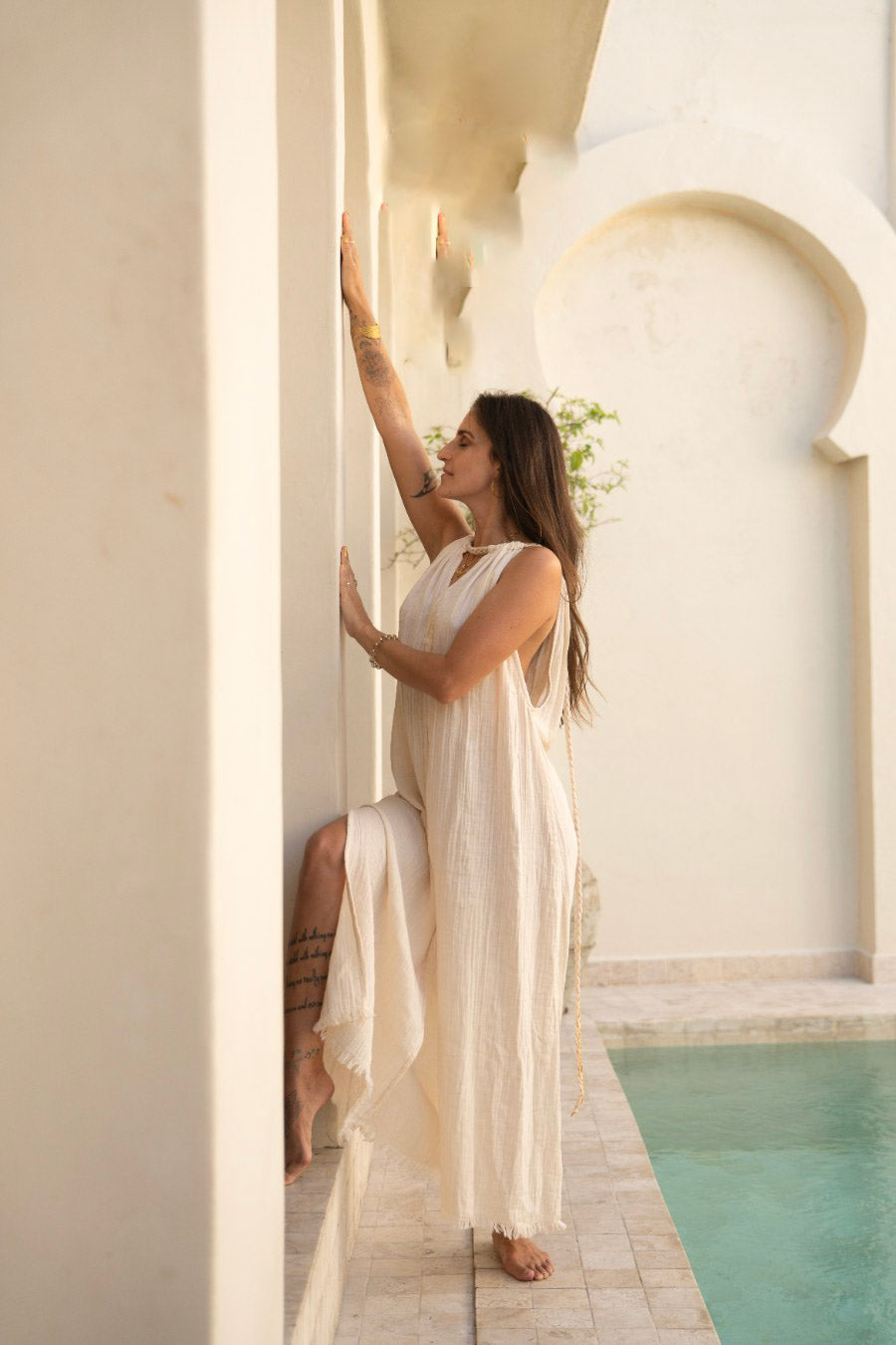 Woman in a white dress standing by a pool with a decorative archway in the background
